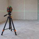 Laser krzyżowy na stabilnym statywie wyświetlający zielone linie na ścianach remontowanego pomieszczenia.